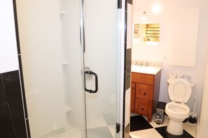 Un baño con mampara de vidrio, inodoro y lavabo con armarios de madera.