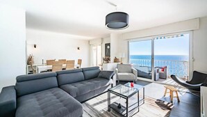 A modern living room with a large gray sectional sofa, a glass coffee table, and a view of the sea through large sliding doors. - Magnifique 3 Pieces Vue Mer Cannes (Cannes)