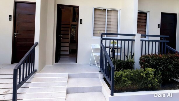 A staircase leading to a building entrance with a white chair and a small garden area. - Prime World District Condo (Lapu-Lapu)