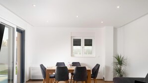 A modern dining area with a wooden table and six chairs, a large window with blinds, a sofa with a laptop, and a potted plant. - Beautiful Villa for 6 Near Zadar Beach (Zadar)