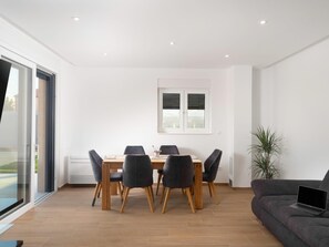 A modern dining area with a wooden table and six chairs, a large window with blinds, a sofa with a laptop, and a potted plant. - Beautiful Villa for 6 Near Zadar Beach (Zadar)