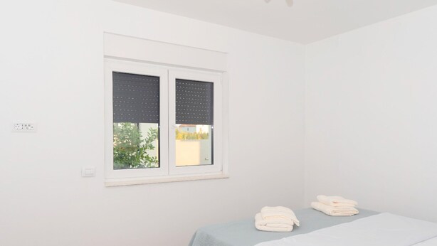 A bedroom with a bed, a window with blinds, and a small table with towels. - Beautiful Villa for 6 Near Zadar Beach (Zadar)