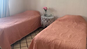 Une petite pièce avec deux lits, une petite table ronde ornée d’un vase de fleurs et un luminaire au plafond.