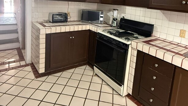 Une cuisine avec des meubles de couleur brun foncé, un four à micro-ondes, une cuisinière et un sol carrelé.