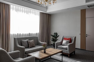 Una sala de estar moderna con un sofá, un sillón y una mesa de centro, una planta en maceta y una puerta al fondo.