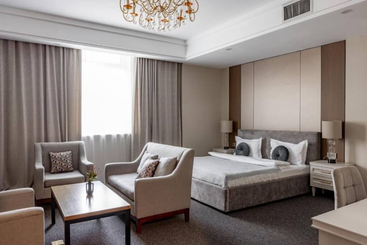 A hotel room with a bed, two armchairs, a coffee table, a desk, and a chandelier.