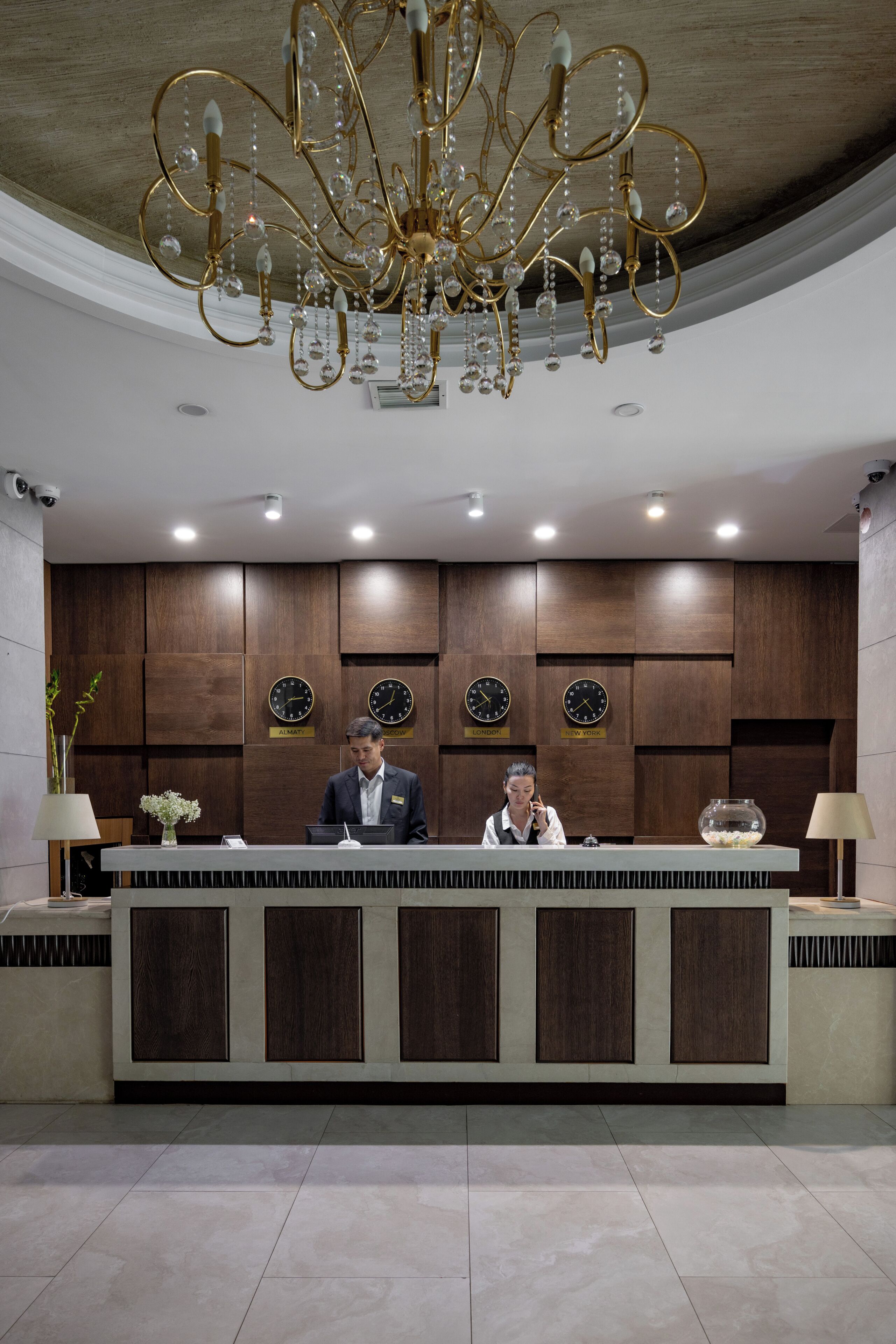 A reception desk with a chandelier, clocks indicating different cities, and a modern interior design.