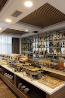 Zona de bufé con distintas estaciones de comida, una exhibición de vinos y licores, y un área de estar con vistas al exterior.
