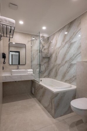 Un baño moderno con pared de mármol, ducha con cerramiento de vidrio, lavabo blanco y retrete.