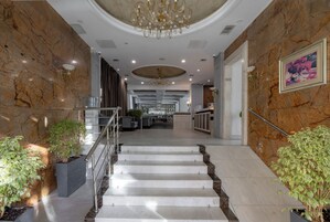 Una imponente escalera conduce a un vestíbulo con paredes de mármol, un candelabro y una zona de bar.