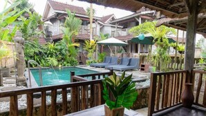 Un espace piscine doté de chaises longues, entouré de plantes tropicales et de bâtiments traditionnels en bois.