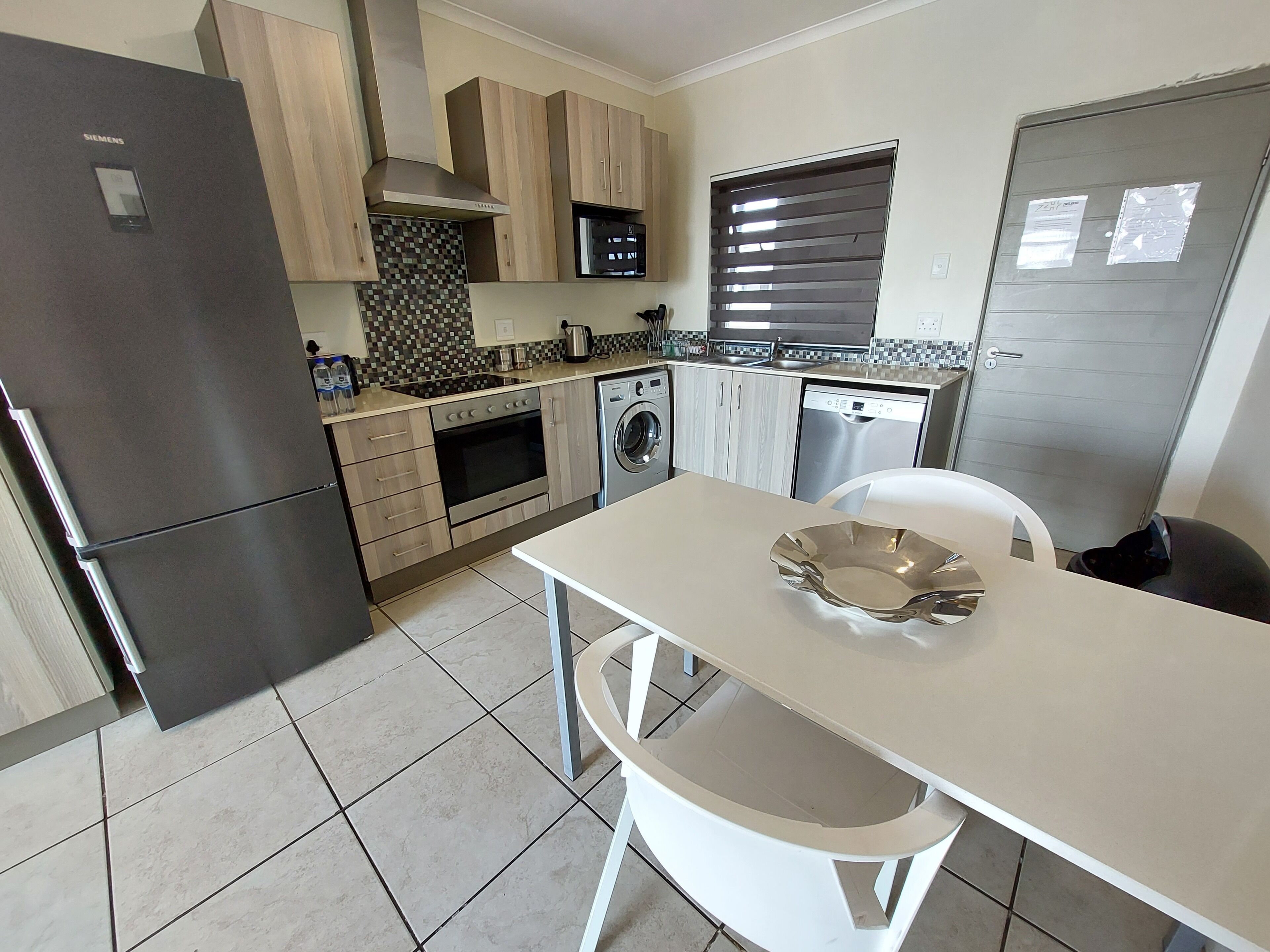 A modern kitchen with a refrigerator, oven, microwave, dishwasher, and a dining area with a table and chairs.