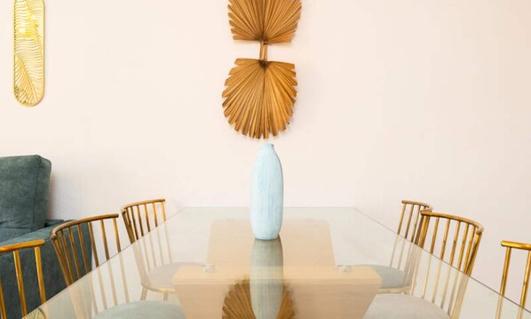 Ein Essbereich mit einem Glastisch, vier Stühlen, einer blauen Vase und zwei Wandbildern.