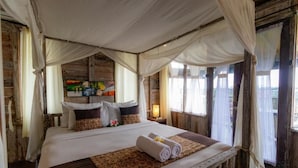 A large bed with a canopy, a bedside table with a lamp, and a view of the outside through a window.