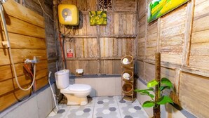 A small bathroom with a toilet, a shower, and a sink. There is a plant in the corner and a wall-mounted fan.
