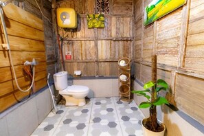 A small bathroom with a toilet, a shower, and a sink. There is a plant in the corner and a wall-mounted fan. - Room-charming Deluxe Room Upper Floor at (Ubud)