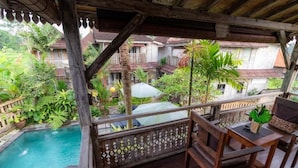 A wooden balcony with a view of a swimming pool and surrounding greenery.