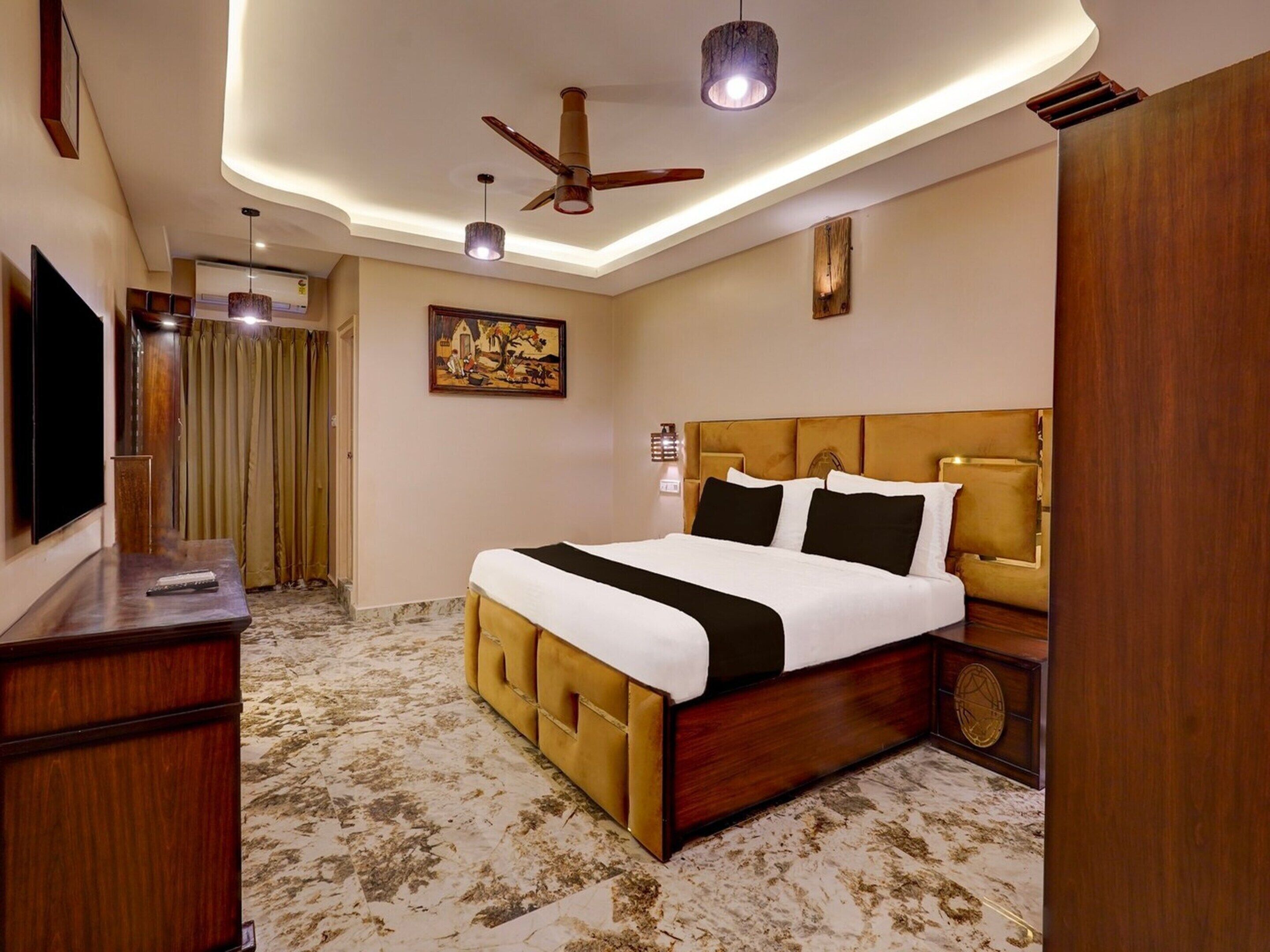 A hotel room with a large bed, a TV, a ceiling fan, and a painting on the wall.