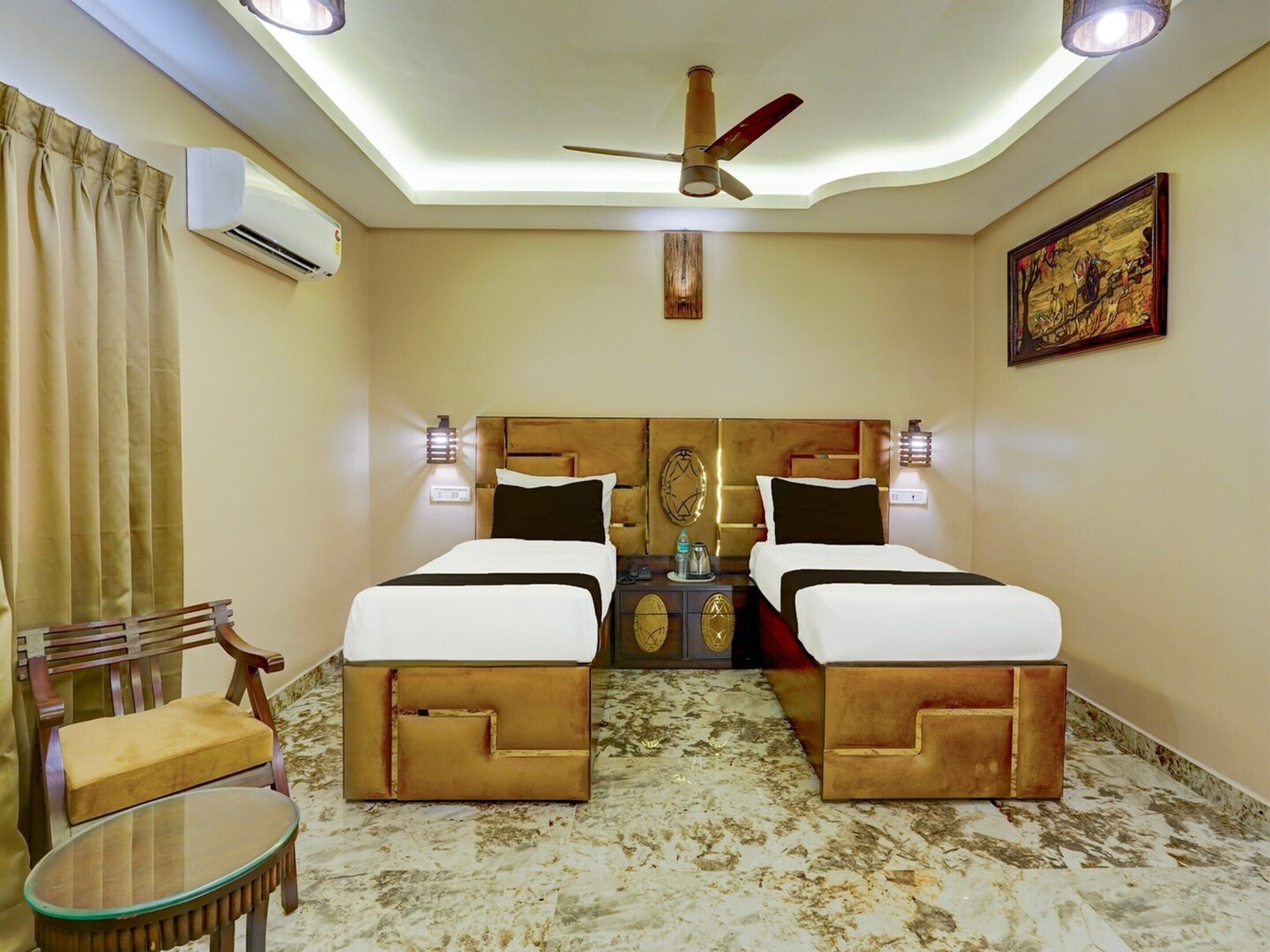 Une chambre d’hôtel avec deux lits, un ventilateur de plafond, un appareil de climatisation, une petite table, une chaise et un tableau au mur.