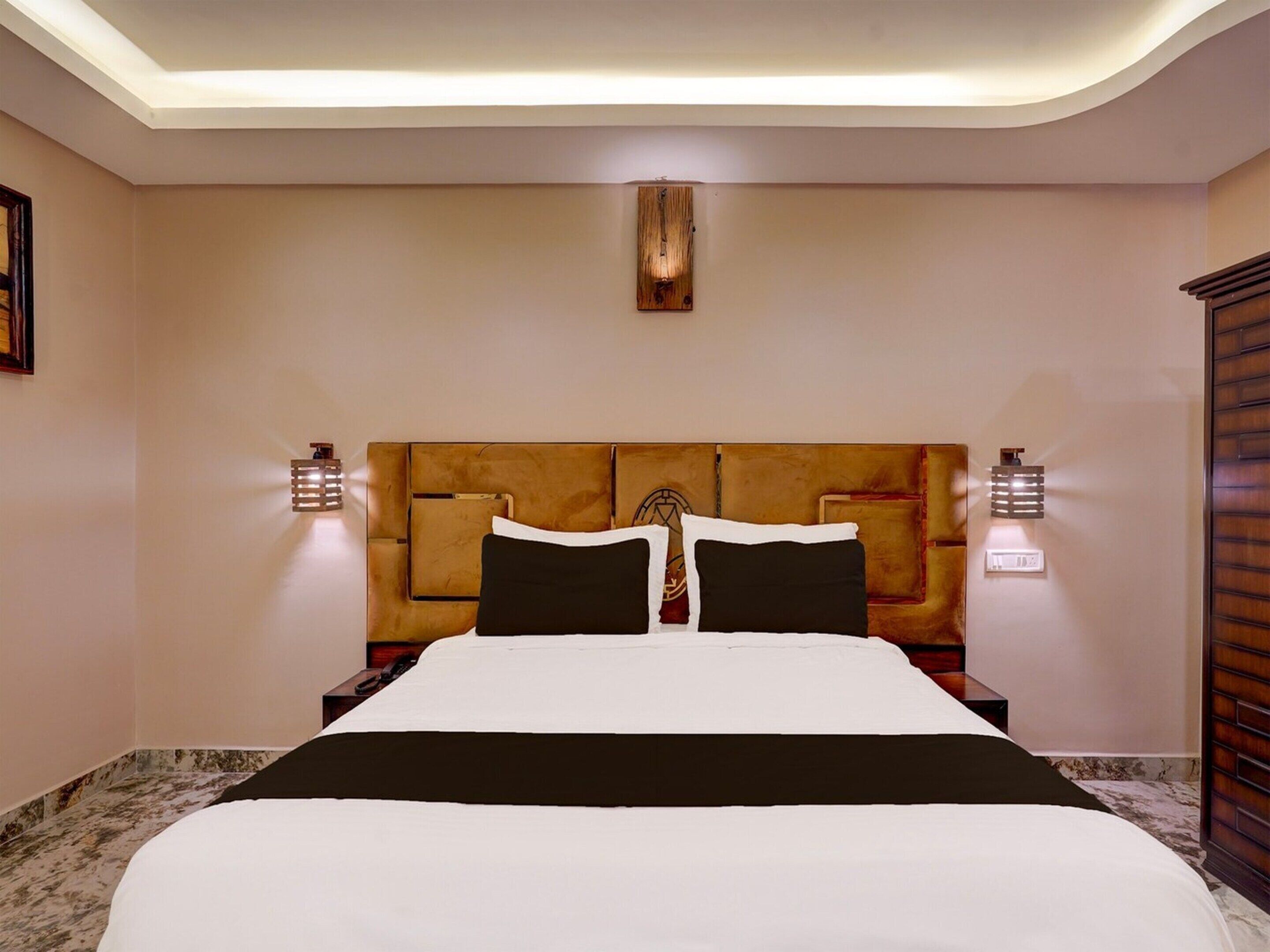 Habitación de hotel con una cama grande, cabecero de madera, dos mesitas de noche e iluminación empotrada.