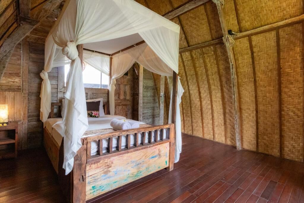 A rustic wooden room with a four-poster bed, a wooden nightstand, and a woven wall.