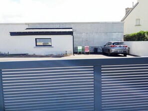 Un espace de stationnement avec une voiture, un bâtiment blanc doté d’une fenêtre et un mur avec une petite fenêtre.