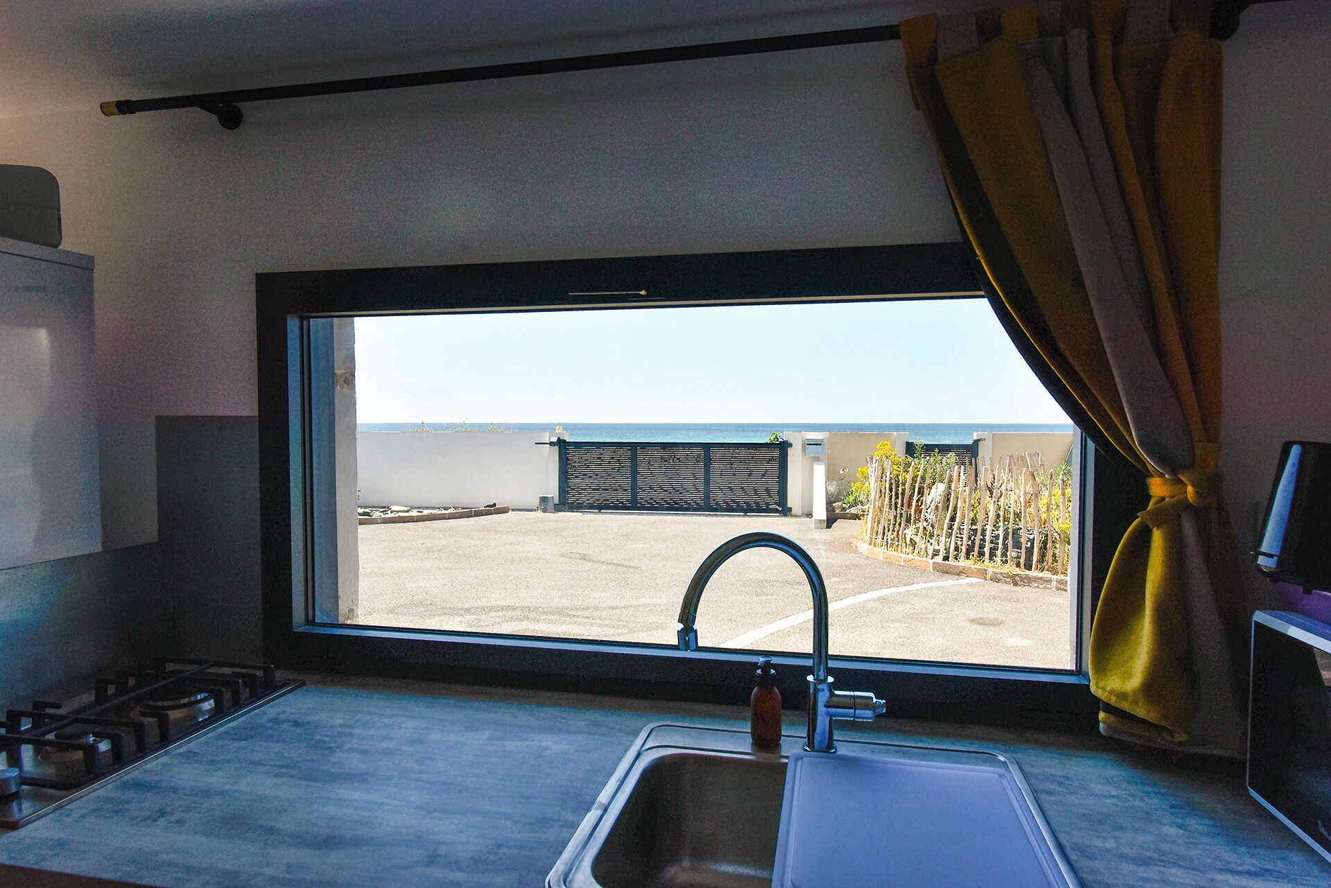 Eine Küche mit einem großen Fenster, einer Spüle und Blick auf einen befestigten Bereich sowie einen Zaun.