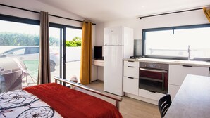 Habitación de hotel moderna con balcón, kitchenette y cama con manta roja.