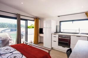 Une chambre d’hôtel moderne avec balcon, kitchenette et un lit recouvert d’une couverture rouge.
