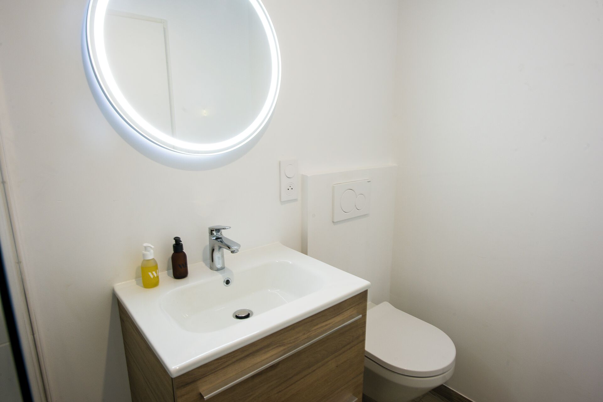 Ein Badezimmer mit weißem Waschbecken, einem Spiegel mit Beleuchtung, einer Toilette und einem Holz-Waschtisch.