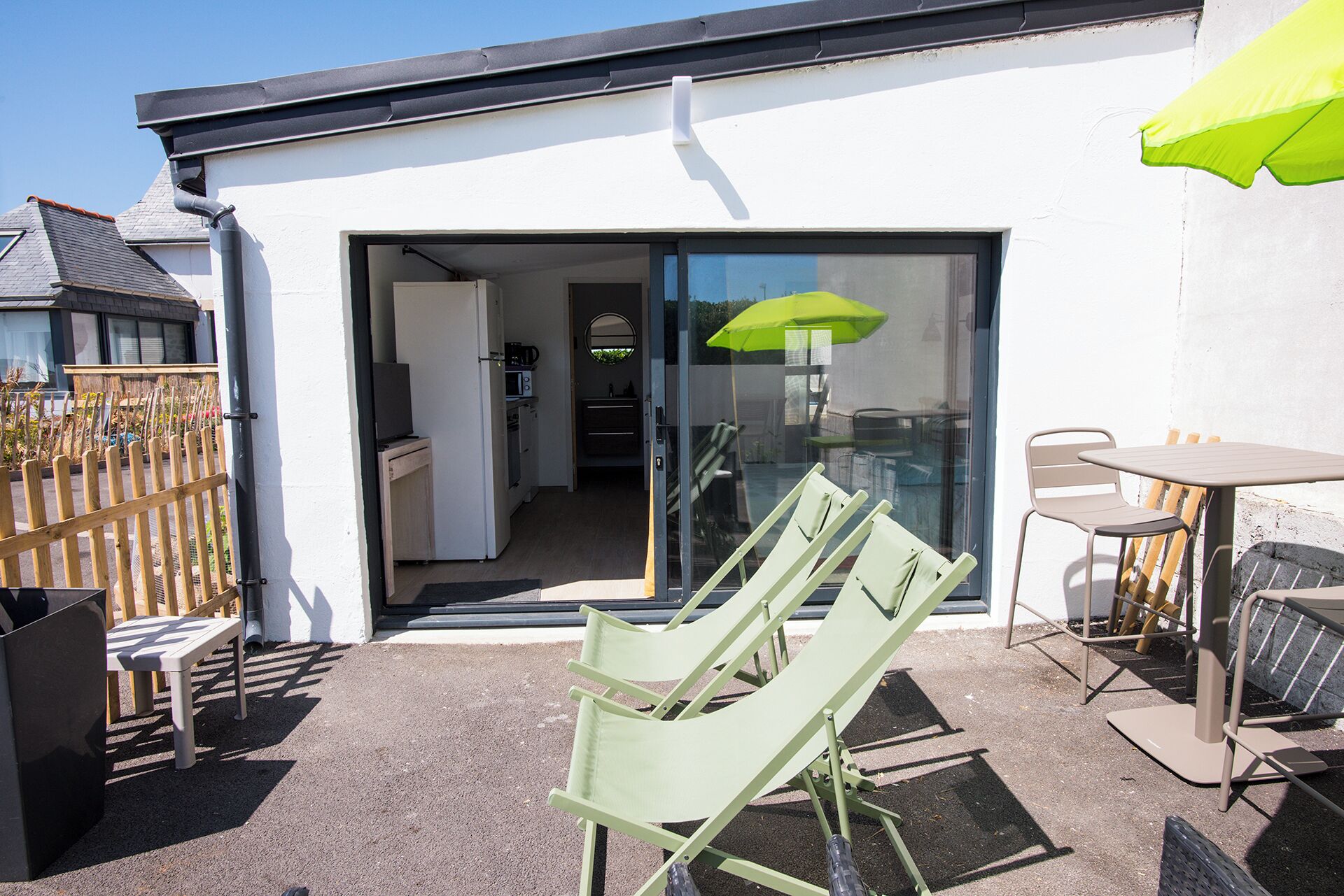 Un patio con mobiliario exterior, una puerta corrediza de vidrio que da a una cocina y un paraguas verde.