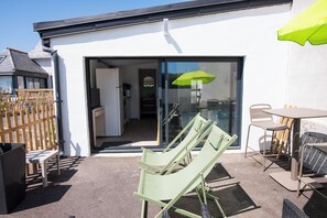 Eine Terrasse mit Gartenmöbeln, eine Glasschiebetür zu einer Küche und ein grüner Sonnenschirm.