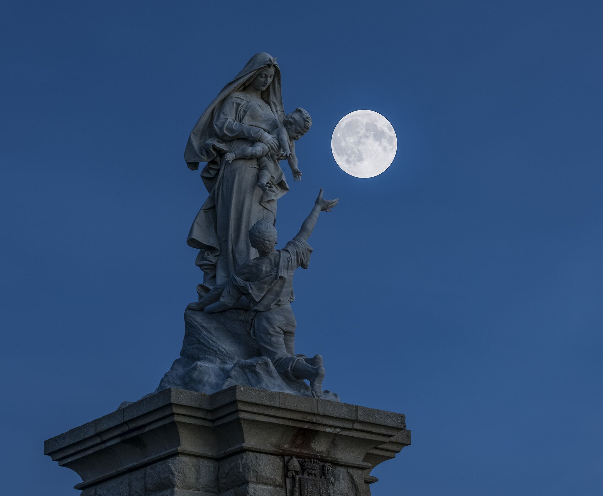 Una estatua de una mujer sosteniendo a un niño, con una luna de fondo.