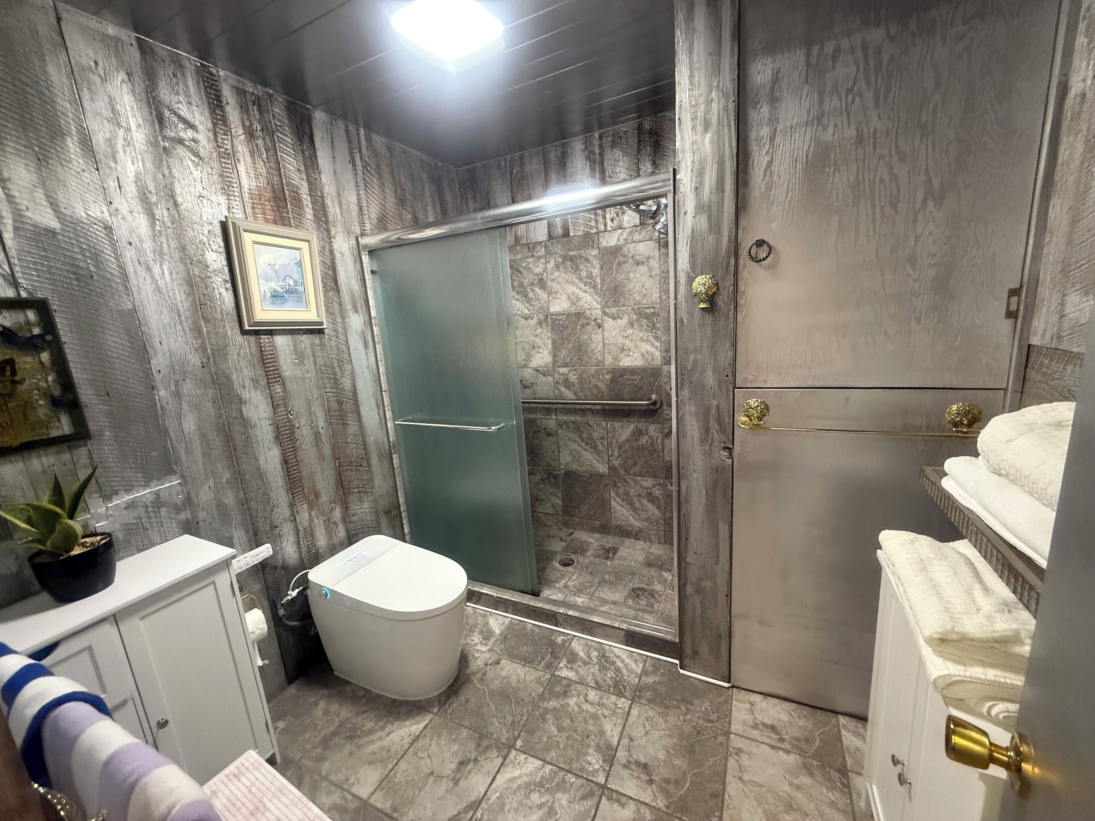 A bathroom with a marble floor, a toilet, a shower with a glass door, and a sink with a towel rack.