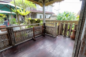 A wooden balcony with a thatched roof, surrounded by lush greenery and traditional buildings. - Room-deluxe Double or Twin Room (Ubud)