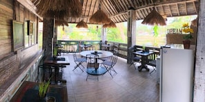 A covered outdoor dining area with a round table and chairs, surrounded by wooden walls and a thatched roof. - Room-deluxe Double or Twin Room (Ubud)
