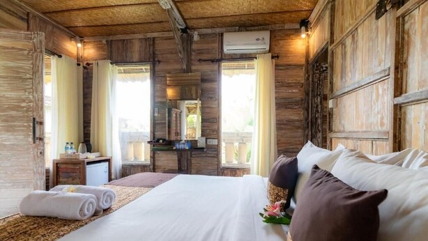 A wooden-themed bedroom with a bed, pillows, a nightstand, and a mirror. - Room-deluxe Double or Twin Room (Ubud)