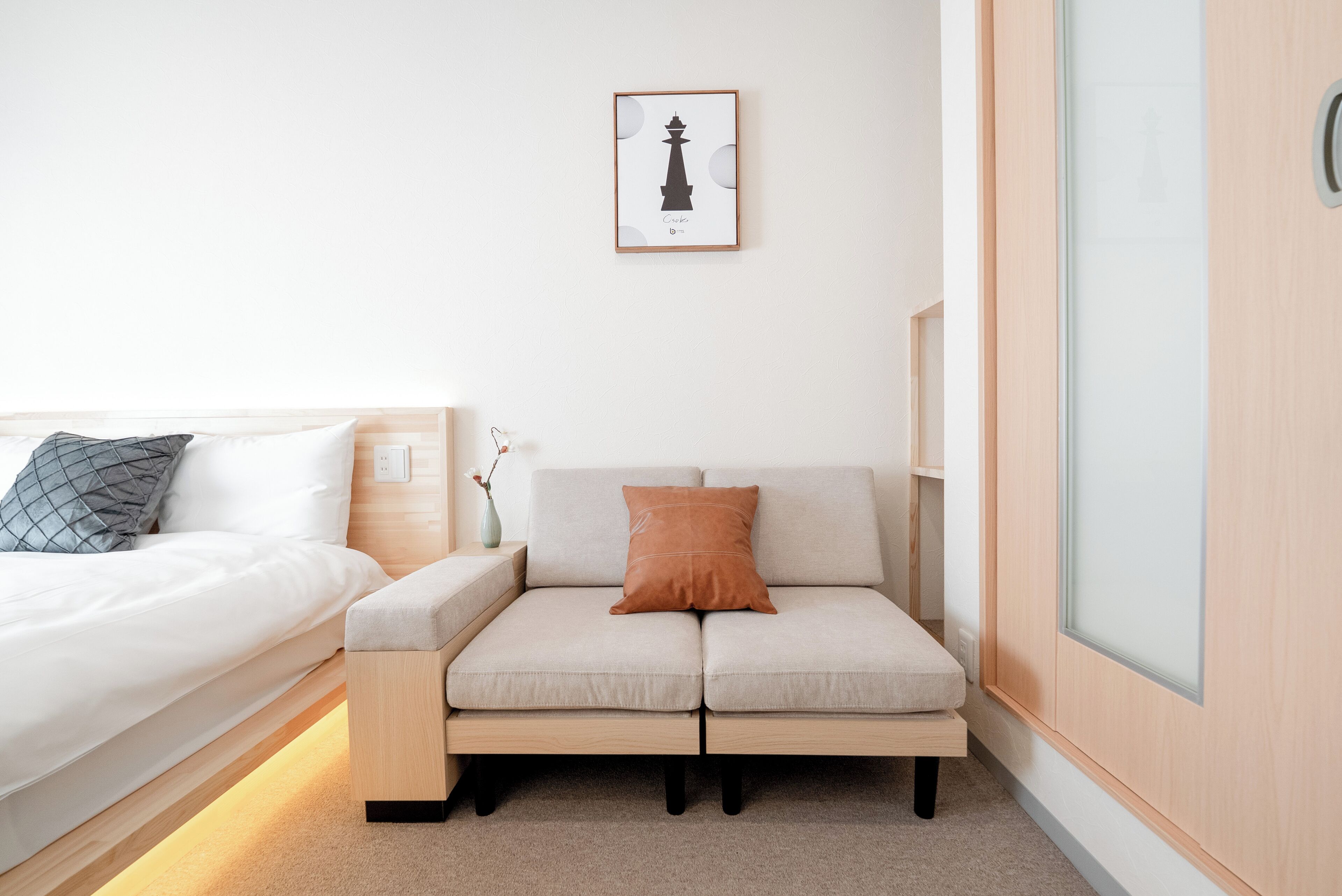 Une chambre à coucher moderne avec un lit, un canapé, une œuvre d’art encadrée accrochée au mur et un meuble en bois.