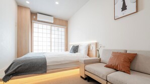 A modern bedroom with a bed, a sofa, a bedside table, and a window with a view. - b&Kuromon 3 (Osaka)