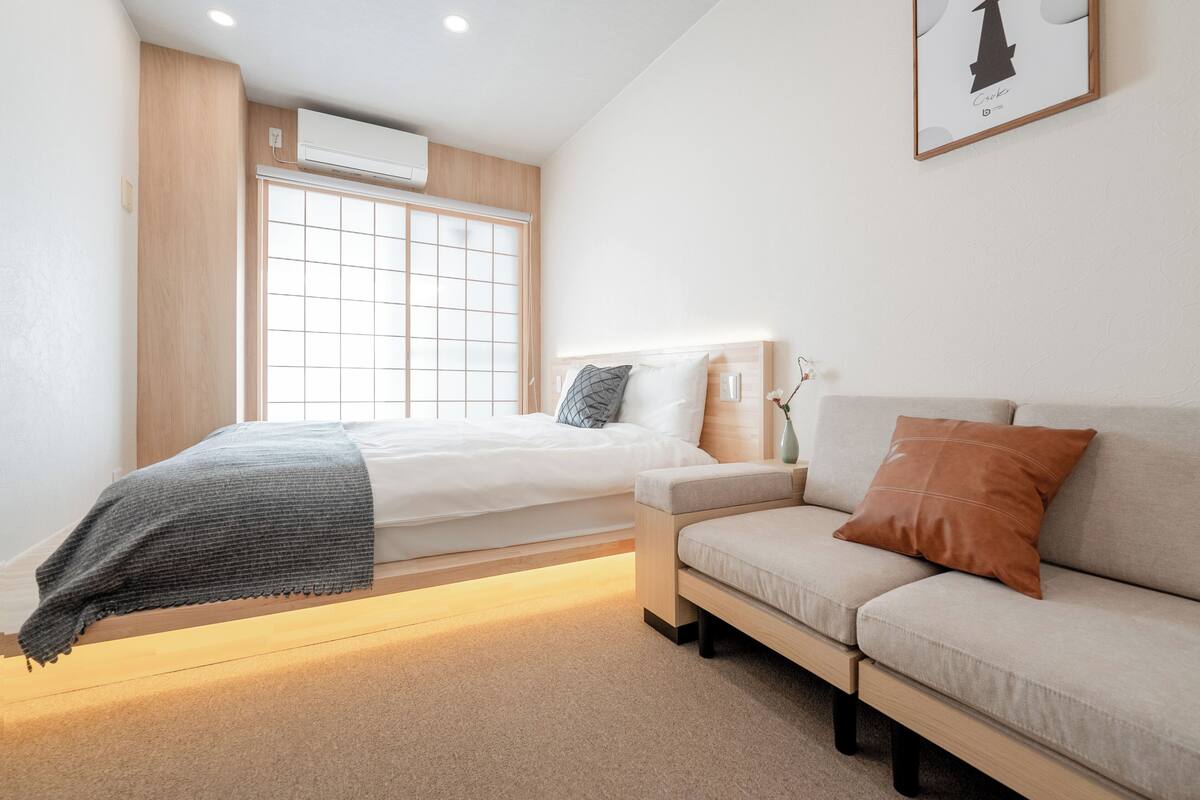 A modern bedroom with a bed, a sofa, a bedside table, and a window with a view.