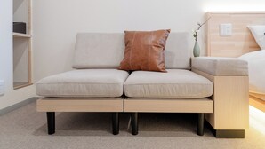 A modern sofa with a brown pillow, a wooden side table with a vase, and a light-colored wall. - b&Kuromon 3 (Osaka)