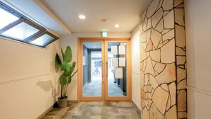 A hallway with a stone wall, a potted plant, and a door leading to a room. - b&Kuromon 3 (Osaka)