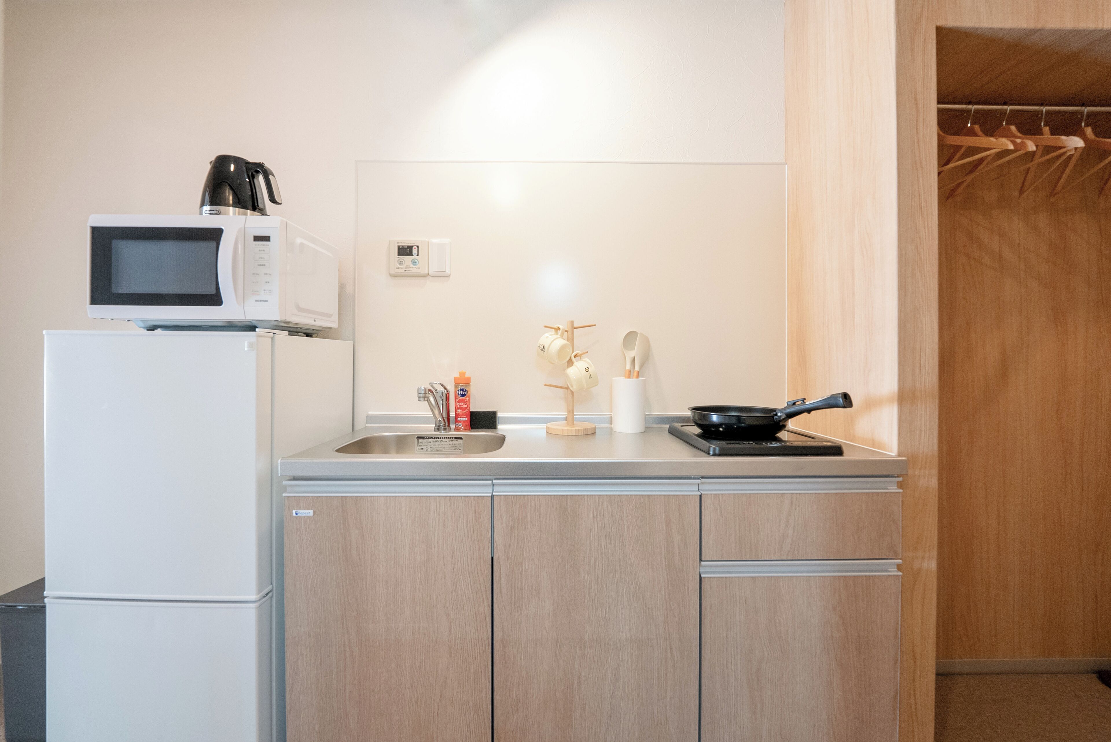 Una cocina compacta con microondas, cafetera y un lavamanos pequeño.