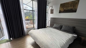 A bedroom with a large bed, a view of the outdoors through a window, and a wooden floor. - Gió Homestay Villa (Xuan Huong - Da Lat)