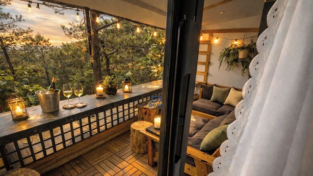 A cozy balcony with wooden flooring, a cushioned seating area, and string lights. - Gió Homestay Villa (Xuan Huong - Da Lat)