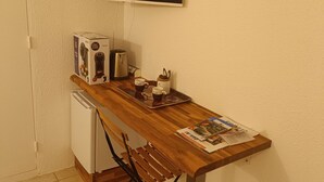 Een compact keukenhoekje met een koelkast, een koffieapparaat en een kleine televisie aan de muur.