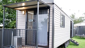 Une maison mobile dotée d’un porche couvert, d’une porte moustiquaire et d’un petit espace extérieur aménagé pour s’asseoir.