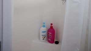 Un espace douche équipé d’un pommeau de douche, d’un rideau et de deux bouteilles de shampoing.