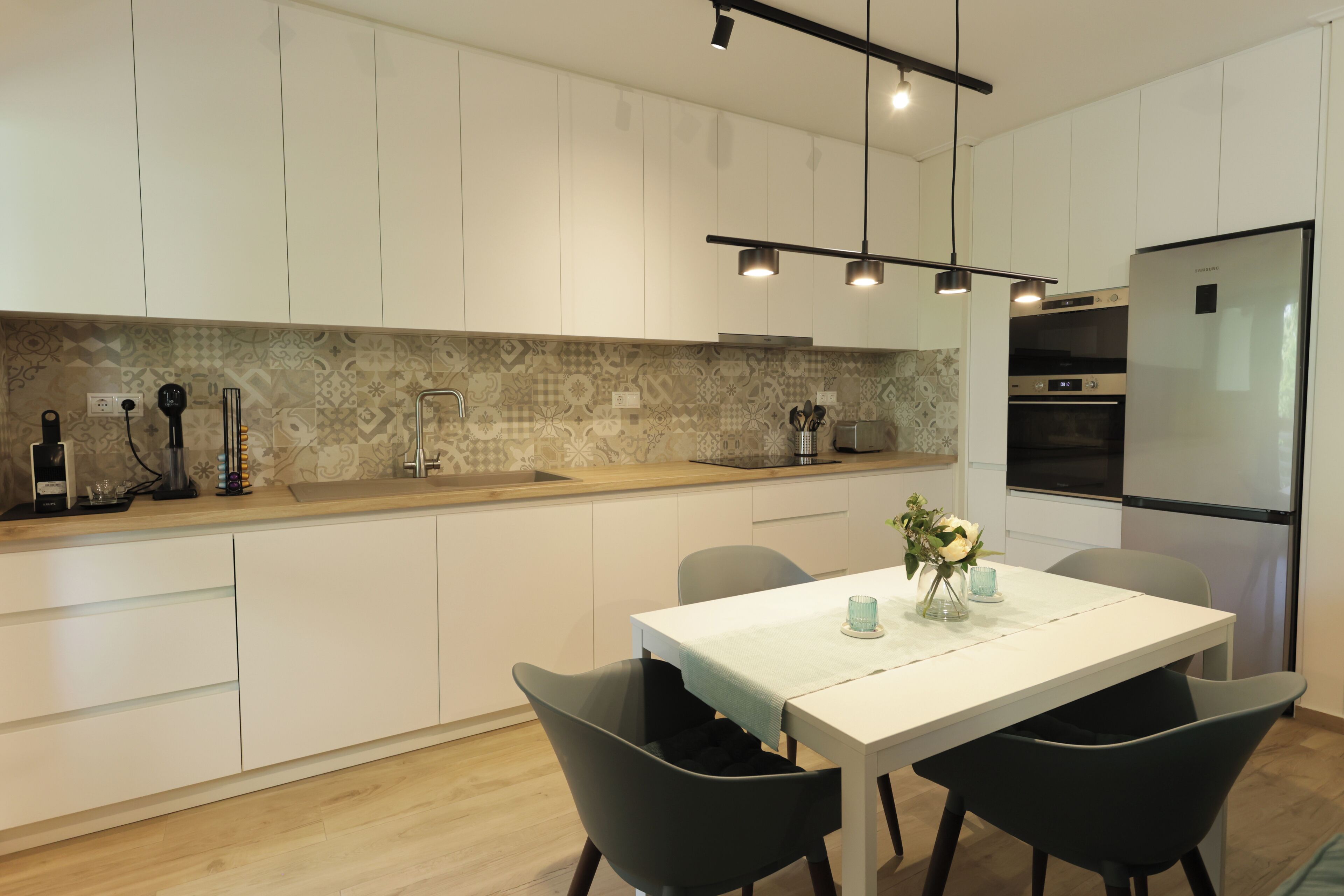 A modern kitchen with white cabinets, a stainless steel refrigerator, and a dining area with a white table and black chairs.