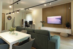 Ein modernes Wohnzimmer mit Essbereich, einem an einer Holzwand montierten Fernseher und einer Couch.